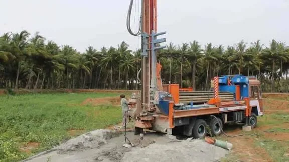 Borewell drilling rig truck in a field lined with coconut palms